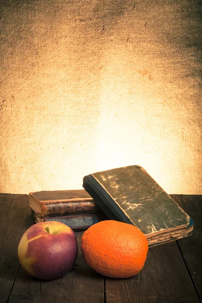 Натюрморт з яблуком, апельсином і стопкою старих книг на старій волі — стокове фото