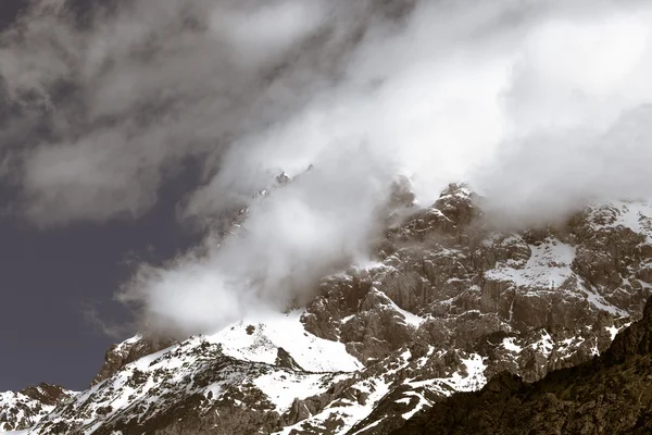 Las nubes yacen en las cumbres cubiertas de nieve de las rocas. Paisaje. Tonelada —  Fotos de Stock