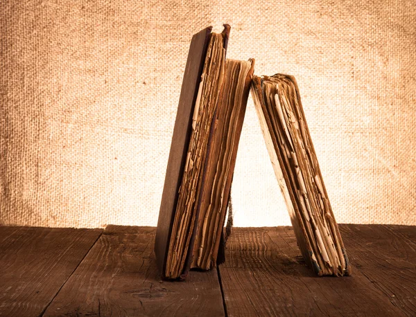 Livres anciens sur une vieille table en bois sur fond de toile de jute — Photo