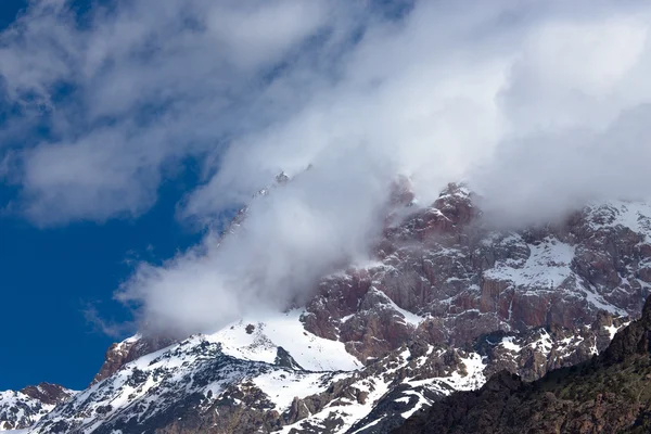 Las nubes yacen en las cumbres cubiertas de nieve de las rocas. Paisaje —  Fotos de Stock