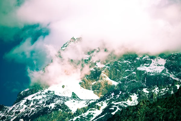 Las nubes yacen en las cumbres cubiertas de nieve de las rocas. Paisaje. Tonelada —  Fotos de Stock