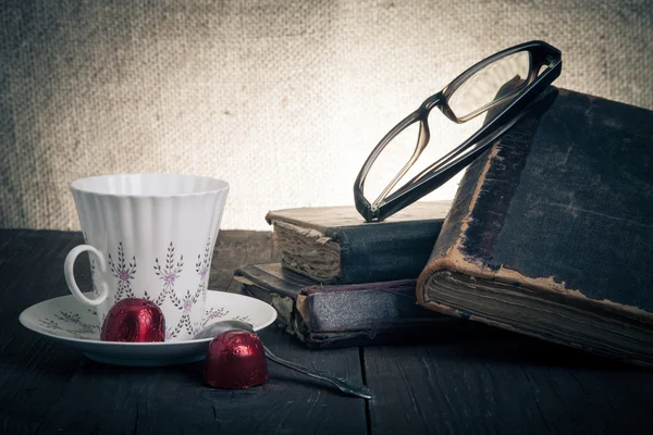 Cup of coffee, shokolad, glasses and stack of old books on the o — Stock Photo, Image