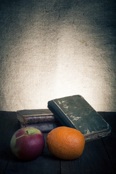 Still life with apple, orange and a stack of old books on old wo — Stock Photo, Image