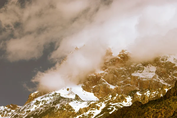 Des nuages se trouvent sur les sommets enneigés des rochers. Paysage. Tonne — Photo