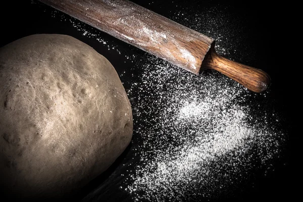 Dough, rolling pin and flour on a black background. Toned — Stock Photo, Image