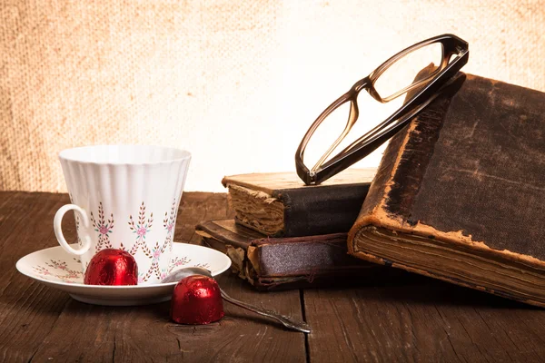 Šálek kávy, shokolad, brýle a zásobník starých knih na o — Stock fotografie