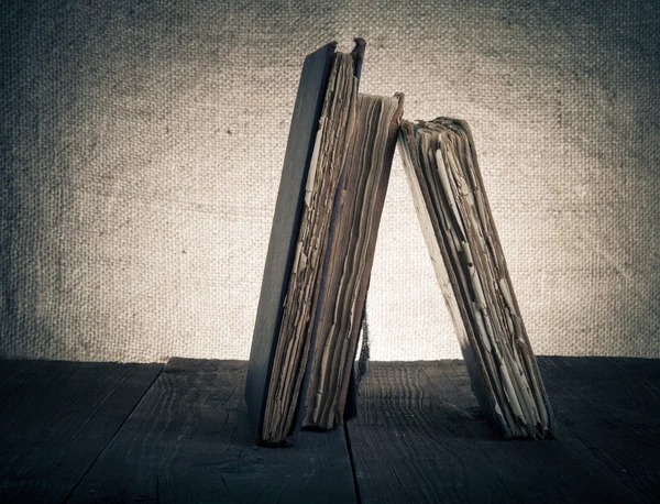 Régi könyvek a régi fából készült asztal, a háttérben a zsákvászon. — Stock Fotó