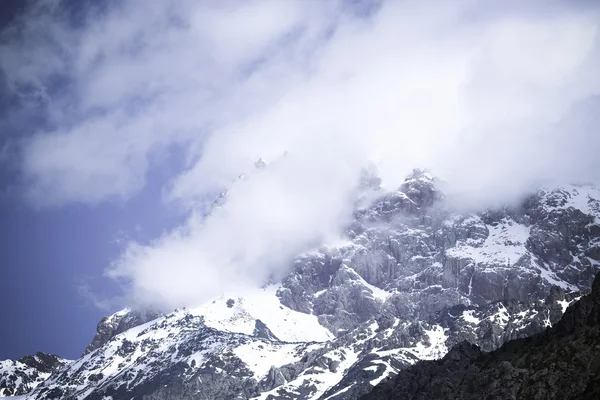 Clouds lie on the snow-covered tops of the rocks. Landscape. Ton — Stock Photo, Image