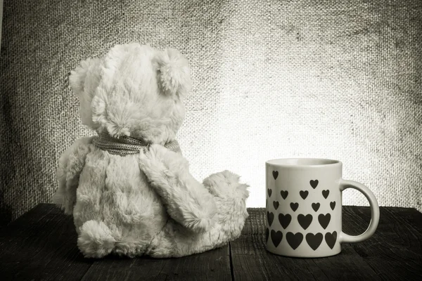 Teddybär sitzt auf dem alten Holztisch. Becher mit Herzen. — Stockfoto
