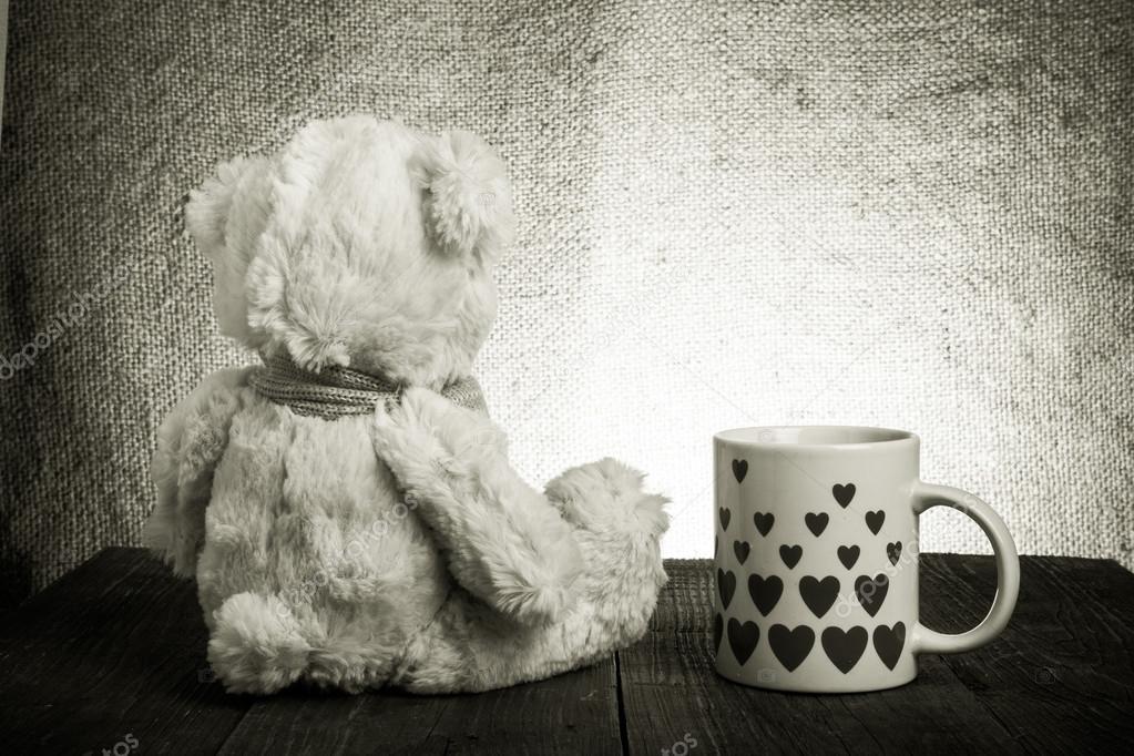 Teddy bear is sitting on the old wooden table. Mug with hearts.