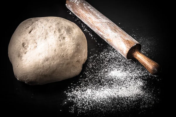 Dough, rolling pin and flour on a black background. Toned — Stock Photo, Image