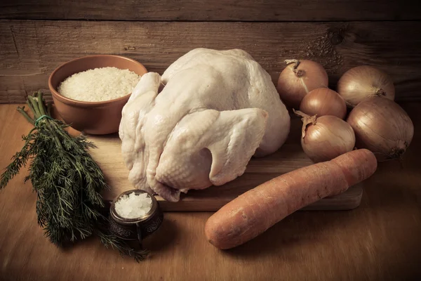 Целый сырой цыпленок, лук, морковь, укроп, рис, соль на деревянном пакете — стоковое фото