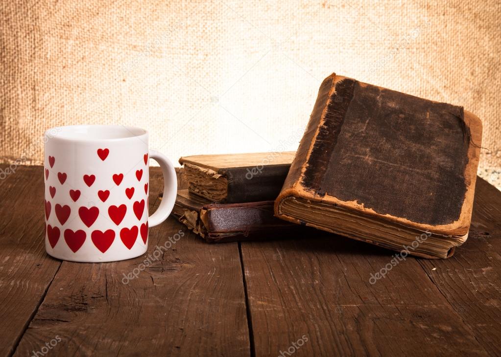old books and a cup with hearts on a wooden table