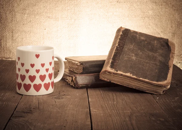 Old books and a cup with hearts on a wooden table — Stock Photo, Image