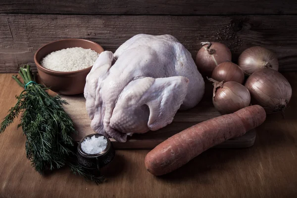 Целый сырой цыпленок, лук, морковь, укроп, рис, соль на деревянном пакете — стоковое фото