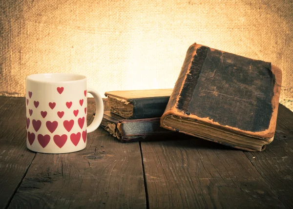 Old books and a cup with hearts on a wooden table — Stock Photo, Image