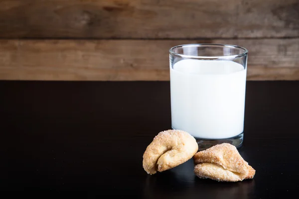 Two cookies and glass of milk on a black table against old woode — Stock Photo, Image