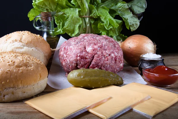 Carne, queso, cebollas, hierbas, sal, ketchup en una mesa de madera — Foto de Stock