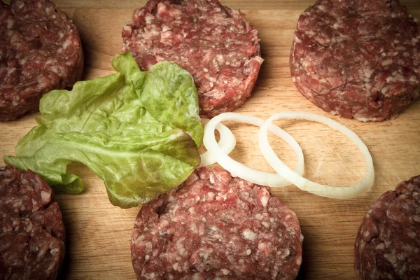 Ruwe kotelet van gehakt vlees met blad van salade en ringen van UI — Stockfoto