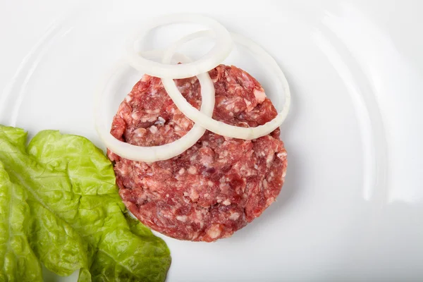 Chuleta cruda de carne picada con hoja de ensalada y aros de cebolla —  Fotos de Stock