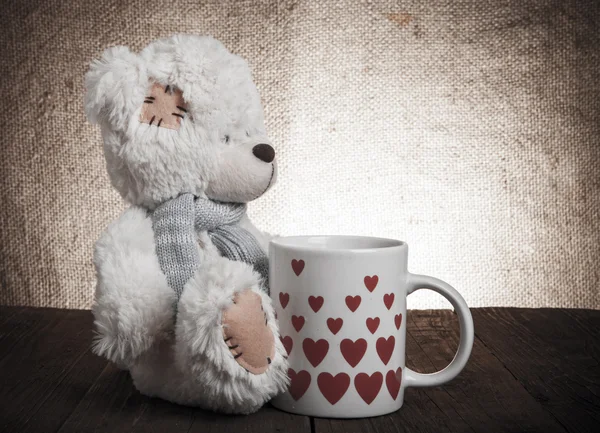 Urso com um copo com corações no fundo do saque — Fotografia de Stock