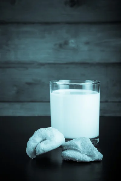 Two cookies and glass of milk on a black table against old woode — Stock Photo, Image