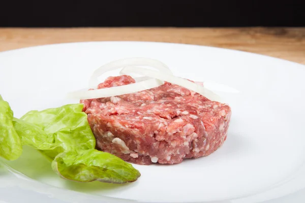 Chuleta cruda, cebolla y ensalada en un plato blanco —  Fotos de Stock