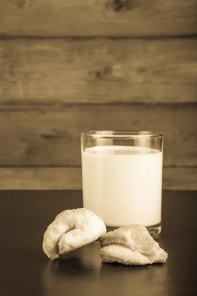 Two cookies and glass of milk on a black table against old woode — Stock Photo, Image