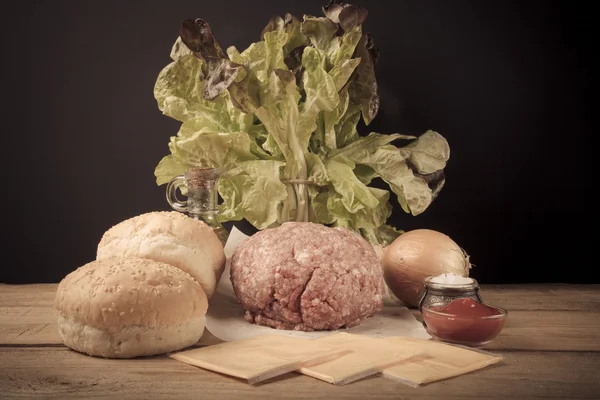 Carne, queso, cebollas, hierbas, sal, ketchup en una mesa de madera — Foto de Stock