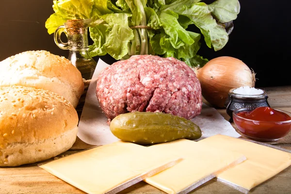 Carne, queso, cebollas, hierbas, sal, ketchup en una mesa de madera — Foto de Stock