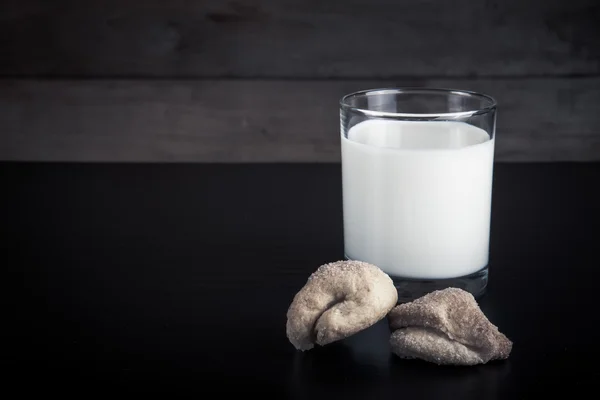 Two cookies and glass of milk on a black table against old woode — Stock Photo, Image