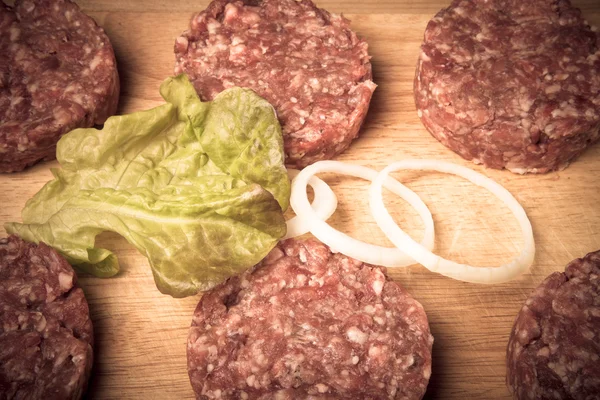 Ruwe kotelet van gehakt vlees met blad van salade en ringen van UI — Stockfoto