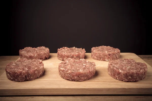 Chuleta cruda de carne picada en una tabla de cortar de madera en bac negro — Foto de Stock