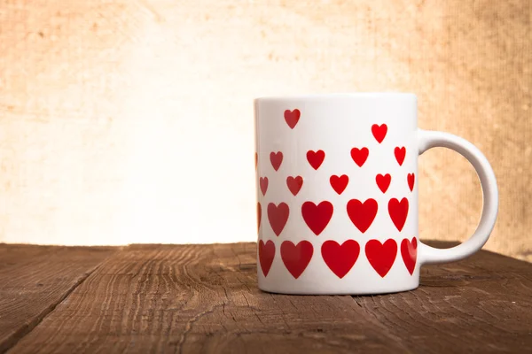 Witte mok met hartjes op oude houten tafel tegen de achtergrond — Stockfoto