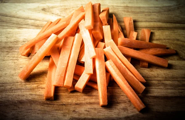 A bunch of pieces of carrots on a wooden cutting board. Toned — Stock Photo, Image