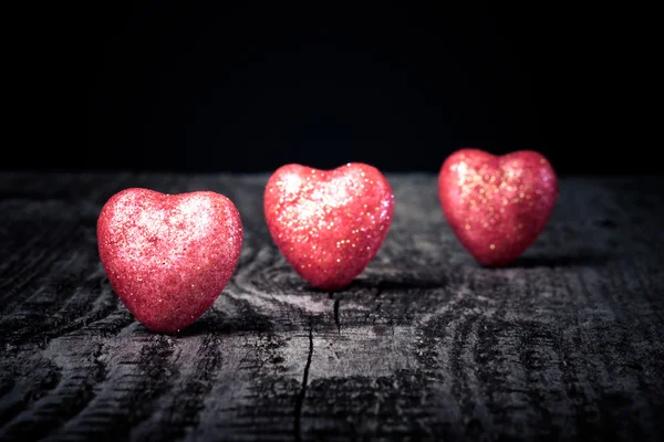 Tres brillantes corazones rojos sobre un viejo fondo de madera. Tonificado — Foto de Stock