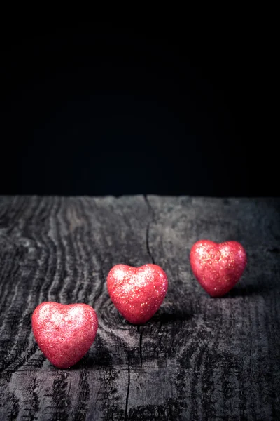 Tres brillantes corazones rojos sobre un viejo fondo de madera. Tonificado — Foto de Stock