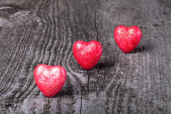 Drie glimmende rode harten op oude houten achtergrond — Stockfoto