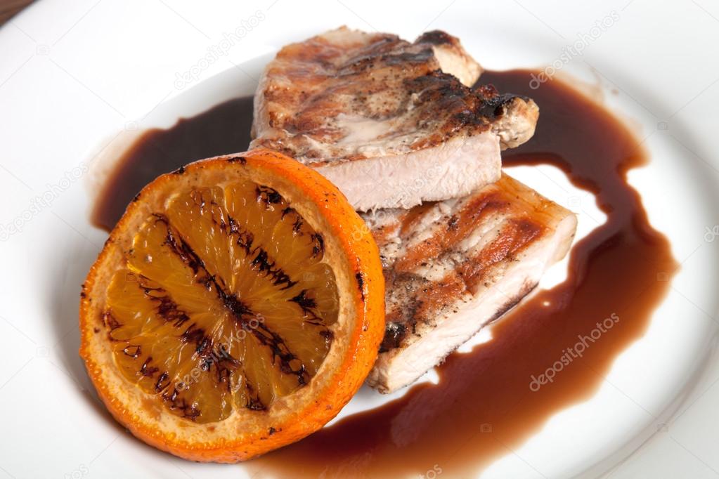 Grilled meat with orange sauce on a white plate