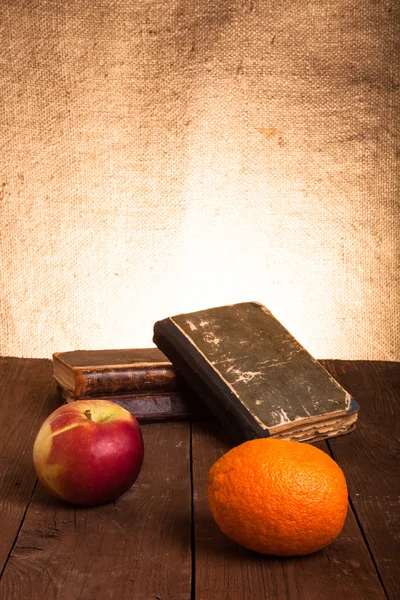 Libros viejos, manzana y naranja tumbados en una vieja mesa de madera — Foto de Stock