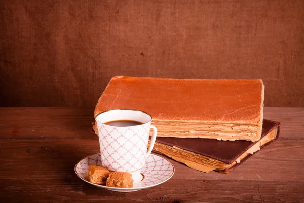 Livres anciens et une tasse de café avec deux bonbons sur un vieux bois — Photo