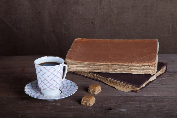 Livres anciens et une tasse de café avec deux bonbons sur un vieux bois — Photo