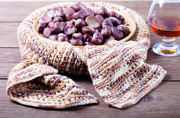 Viele Kastanien in einem gestrickten Schal und Cognac in einem Glas auf alten W — Stockfoto