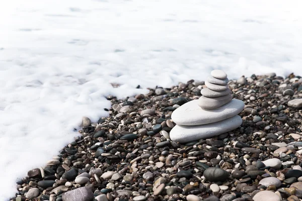 La piramide di ciottoli sulla spiaggia in schiuma di mare — Foto Stock