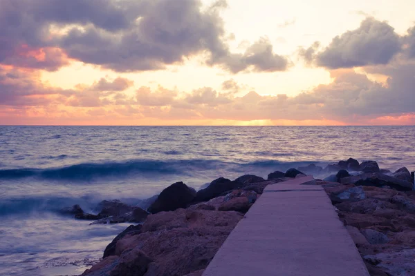 Nubes bajas sobre la costa pedregosa del mar y el muelle. Puesta de sol mar — Foto de Stock