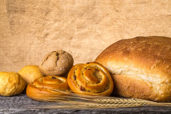 古い木製テーブルの上のパンの品揃えと小麦耳 — ストック写真