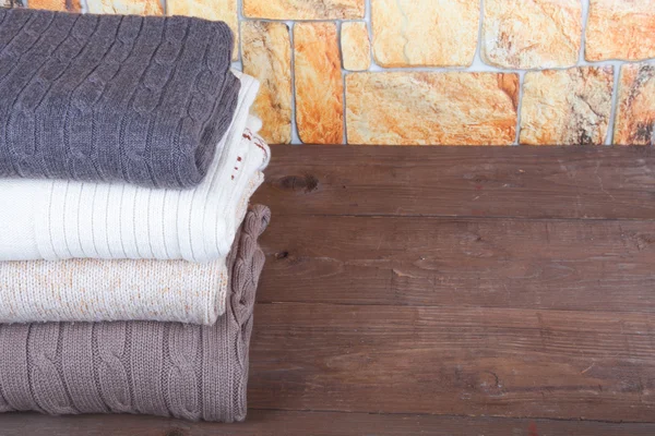 Stack of knitting clothes on wooden table opposite a stony wall — Stock Photo, Image
