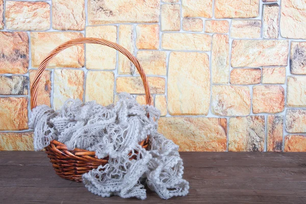 Strickschal im Korb auf Holztisch gegenüber einer steinernen Wand — Stockfoto