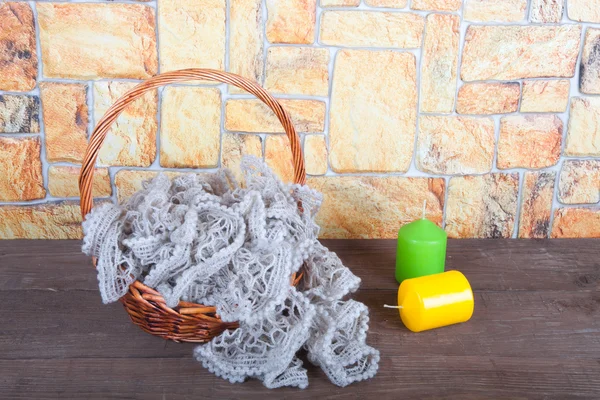 Knitted scarf in the basket and two color candles on wooden tabl — Stock Photo, Image