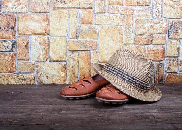 Straw hat and moccasins on a wooden table in front of a stone wa — Stock Photo, Image